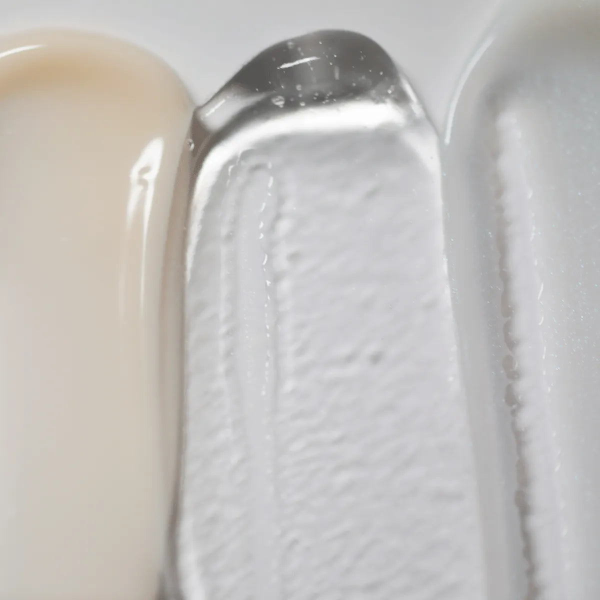 Een close-up afbeelding toont de texturen van Solawaves LightBoost Wand Activating Serum, met romig beige, transparante gel verrijkt met LightBoost technologie, en gladde lichtgrijs/witte crème. De texturen variëren van romig tot gel-achtig, met een glanzende afwerking.